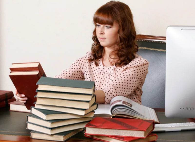 Девушка за столом со стопкой книг